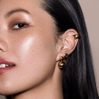 Side of Dark Haired Woman's Face with Focus on Her Ear Wearing 3 Ethical Gold Earrings 