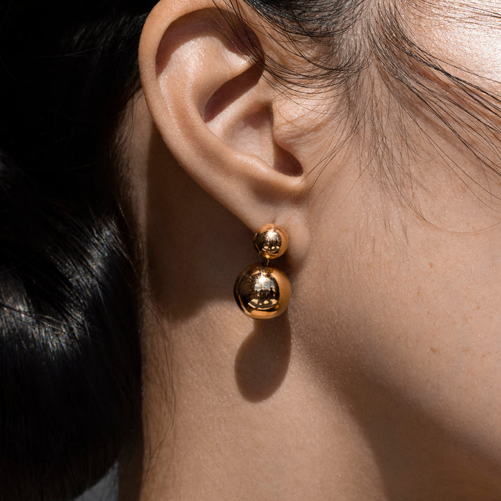 Close up of Ethical Gold Earrings Featuring a Small Gold Sphere Above a Larger Gold Sphere Worn on a Woman's Ear