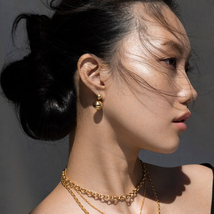 Side Profile of Woman with Dark Hair in an Updo Wearing Ethical Gold Earrings Featuring 2 Small Stacked Spheres