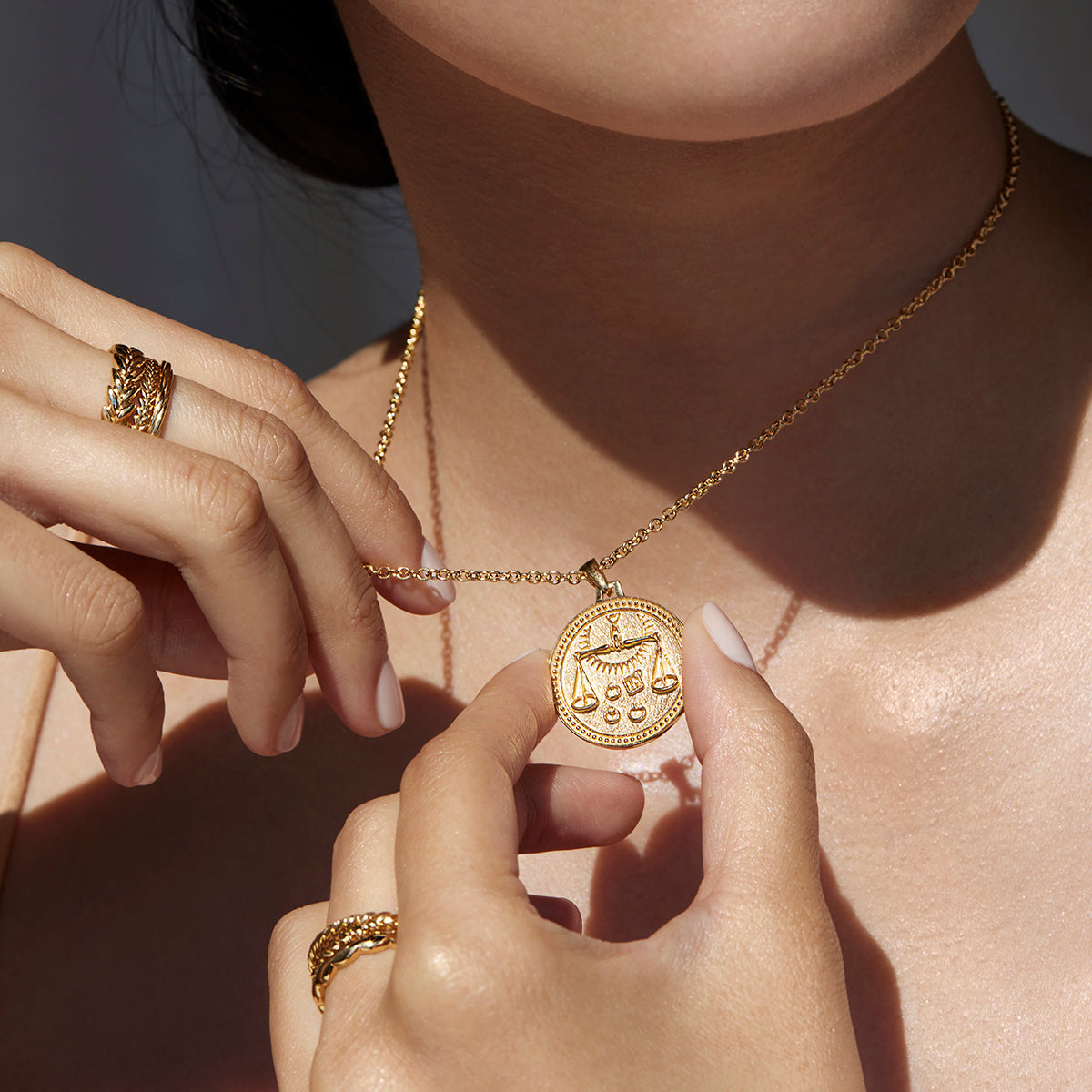 Close Up Woman Wearing Ethical Gold Libra Pendant Necklace, Holding the Pendant Between Her Thumb and Forefinger