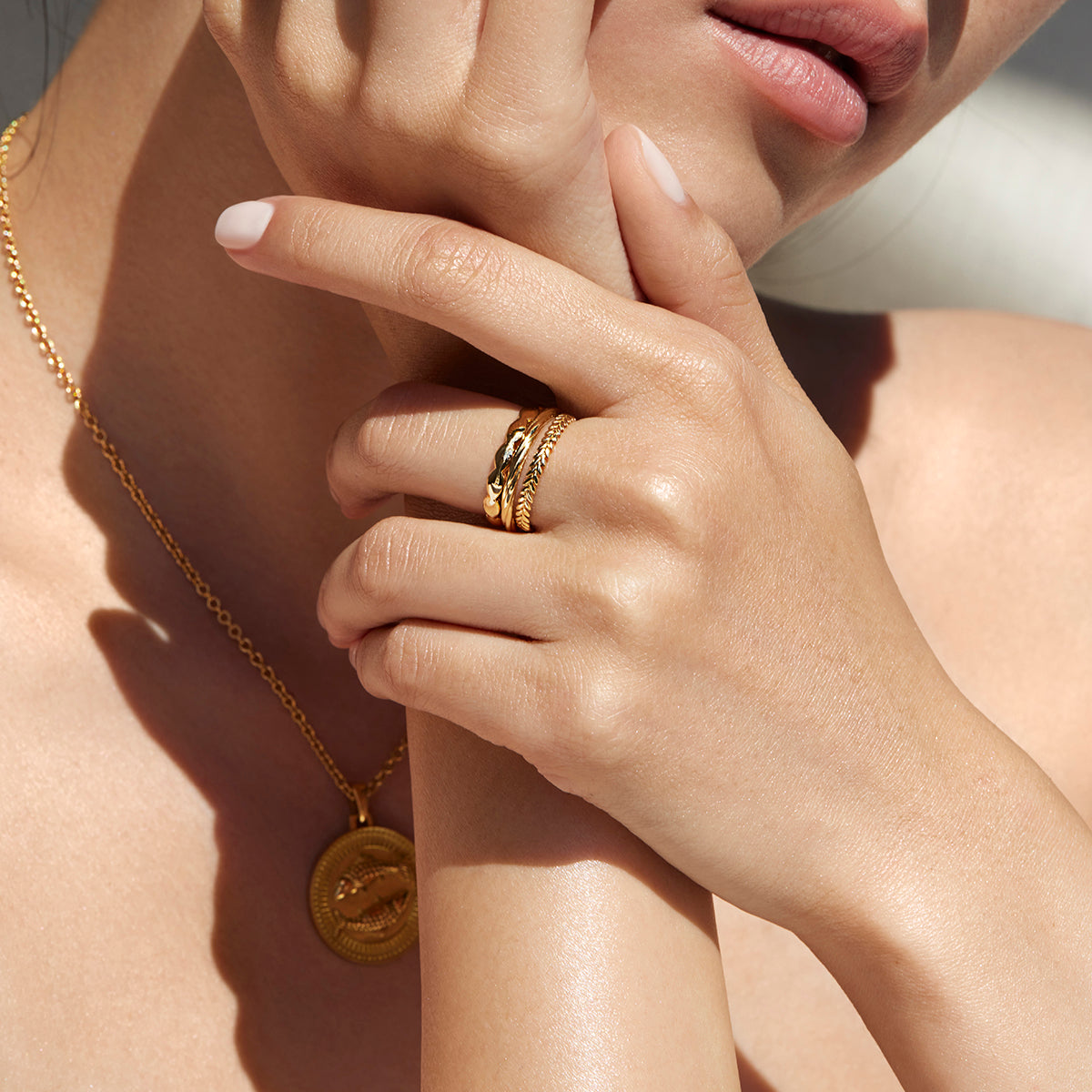 Woman Holding Her Hands by Her Chin Wearing Ethical Gold Band Rings and an Ethical Gold Pisces Pendant Necklace