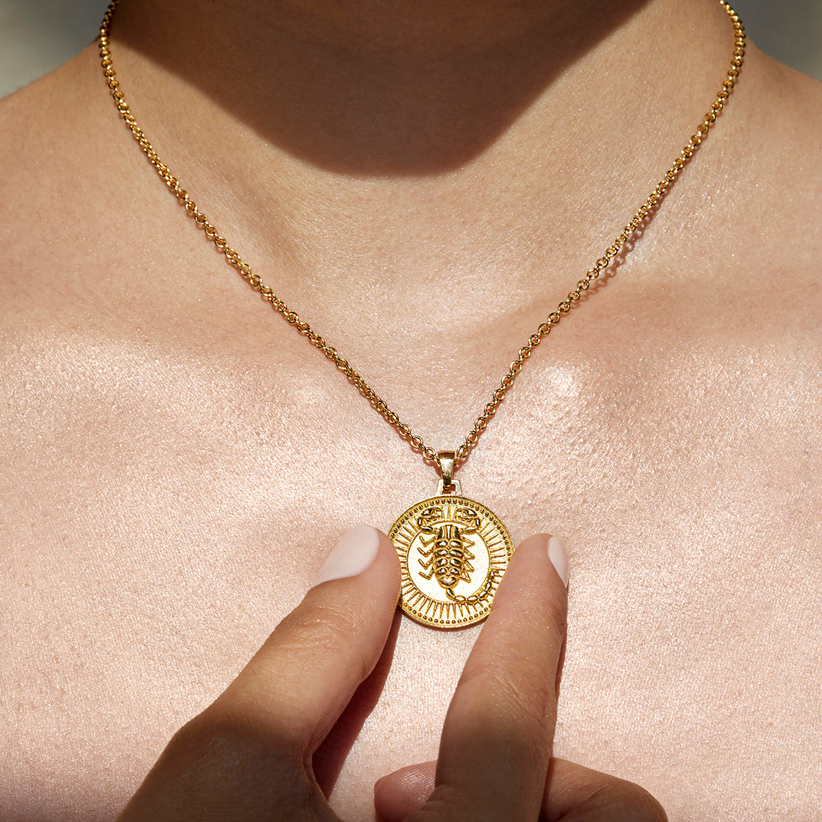 Close Up Woman Wearing Ethical Gold Scorpio Pendant Necklace, Holding the Pendant Between Her Thumb and Forefinger