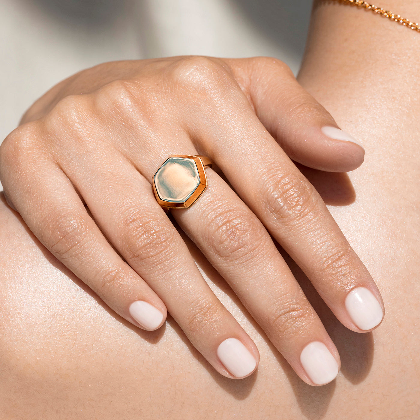 Close Up of Woman's Hand Over Her Shoulder Wearing a Sustainable Gold Ring Featuring a Flat Hexagonal Design at the Top of the Ring on her Middle Finger