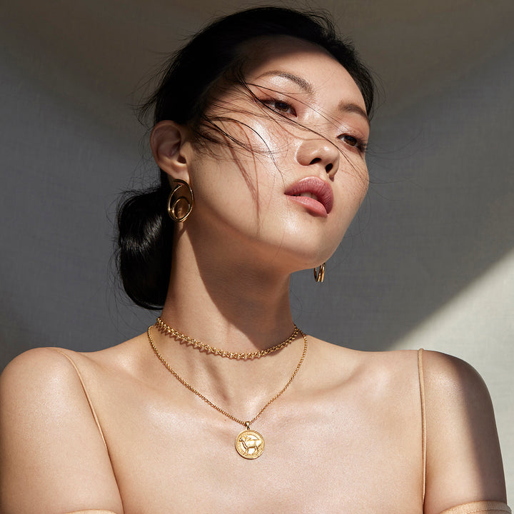Woman Glancing to the Side Wearing Ethical Gold Taurus Pendant, Chain Necklace, Hoop Earrings, and Band Rings