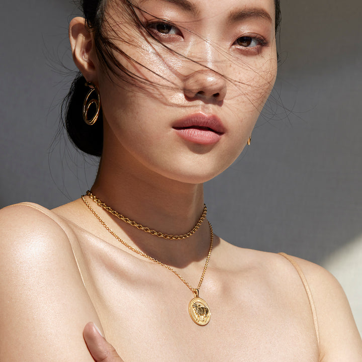 Woman Looking Ahead to the Camera Wearing Ethical Gold Taurus Pendant, Chain Necklace, Hoop Earrings, and Band Rings